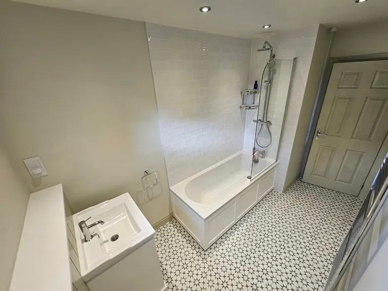 Bathroom with pale green walls, a white bath and patterned floor tiles